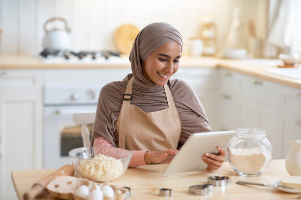 Cheerful Muslim Lady In Hijab Using Digital Tablet In Kitchen