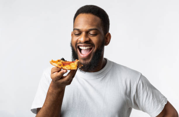 istock Joyful African Millennial Guy Eating Pizza Slice Over White Background 1299556645