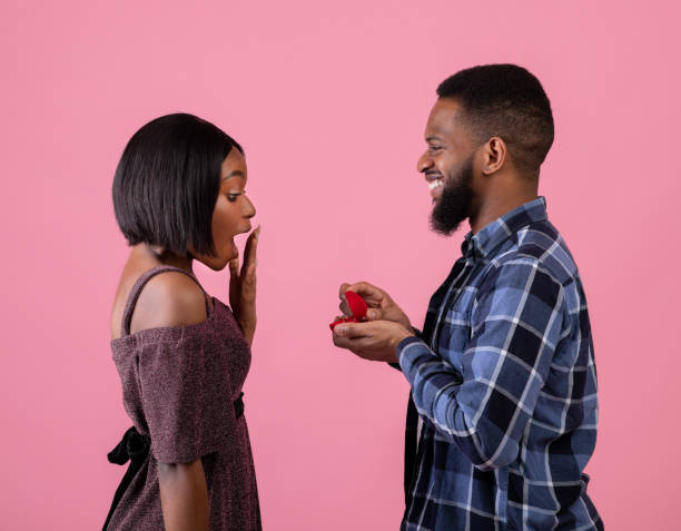 istock Affectionate black man proposing to his girlfriend with diamond ring on pink studio background. Valentine's Day 1299556655