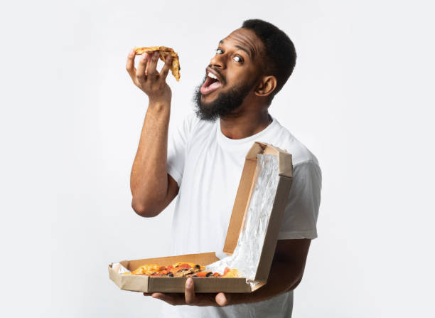 istock Black Guy Eating Pizza Posing With Large Box, White Background 1299556660