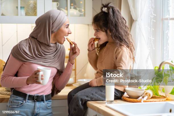 Muslim Mom In Hijab And Her Little Daughter Eating Snacks In Kitchen Stock Photo - Download Image Now