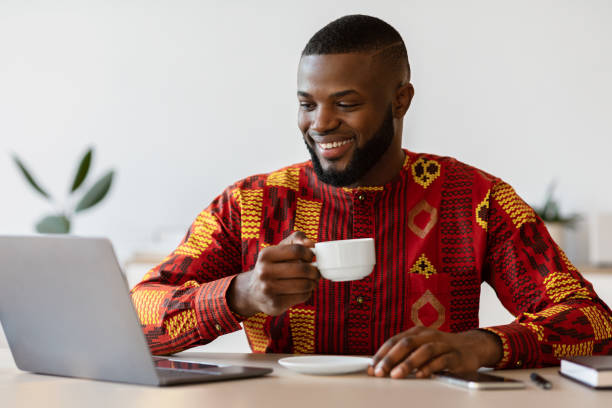 istock Cheerful African Freelancer Guy Using Laptop And Drinking Morning Coffee At Home 1299558578