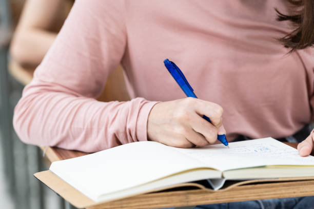 istock Close-up of the university students writing notes on the notebook in the classroom while listening and studying the lecture. Close up of woman's hands writing on notepad placed on wooden desktop 1299558609
