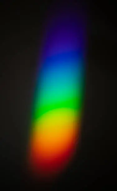 Photo of Rainbow color spectrum effect on wall, light scatter after hitting the glass object on to a dark wall.