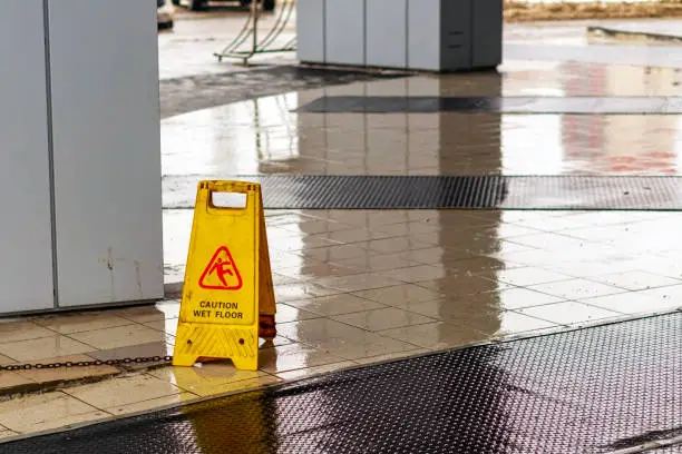 A dirty yellow sign "Wet Floor" stands on the wet tiles on the porch