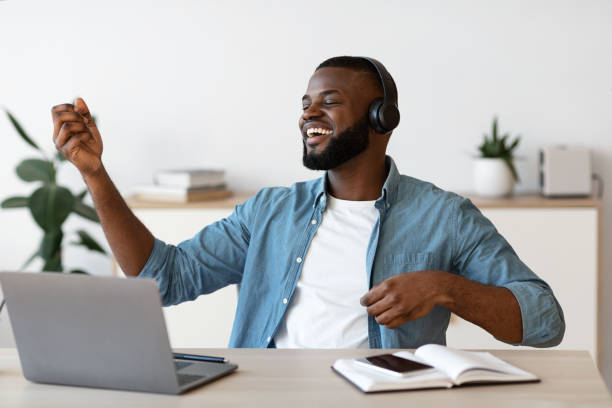 istock Cheerful Black Freelancer Man Listening Music And Playing Virtual Guitar At Workplace 1299561264