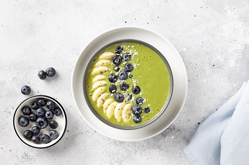 breakfast smoothie bowl with green matcha, banana, almond milk, blueberries. Healthy eating, detox and diet concept. Gray background. top view