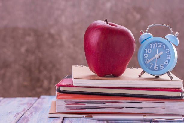 istock Back to school, notebook,alarm clock,red apple,flower on wooden table with blurred background 1299561975