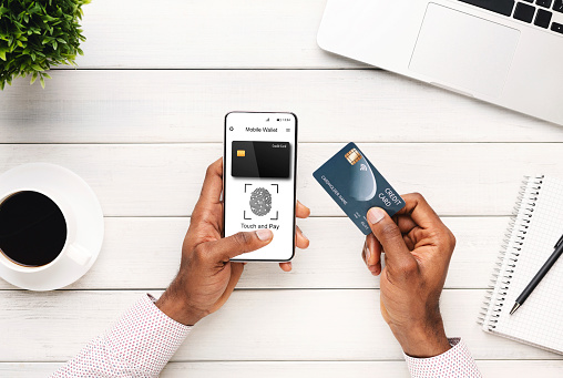 Mobile Wallet Application. Black Man With Phone Holding Credit Card Approving Online Payment With Fingerprint Scanner Sitting At Desk In Office. Financial Safety And Security. Collage, Cropped