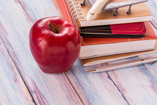 Concept of back to school. Pile of books and red apple on the desk over the blur background.