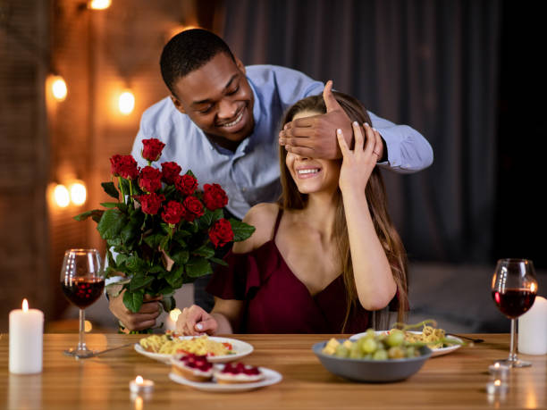 surprise romantique. homme noir heureux couvrant les yeux de petite amie et donnant le bouquet de roses - anniversary couple rose black photos et images de collection