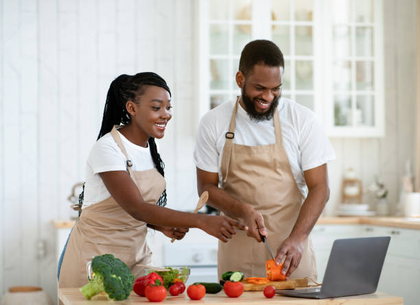 istock Happy African Spouses Using Laptop Computer While Cooking In Kitchen, Searching Recipe 1299564157