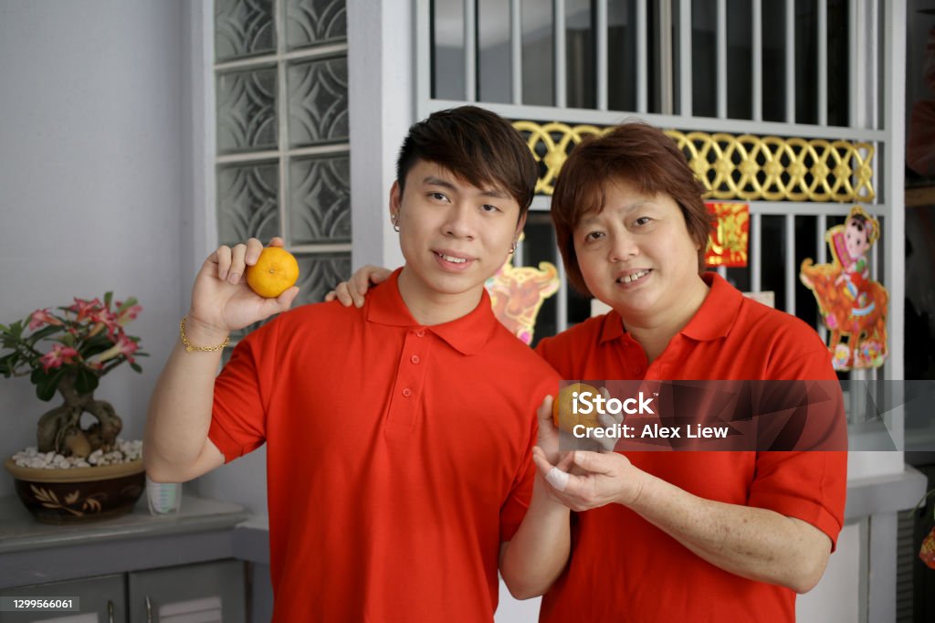 New Normal - Chinese New Year Portrait of an Asian young man holding tangerines (mandarin oranges) with his mother at home for Chinese New Year celebration. 20-24 Years Stock Photo