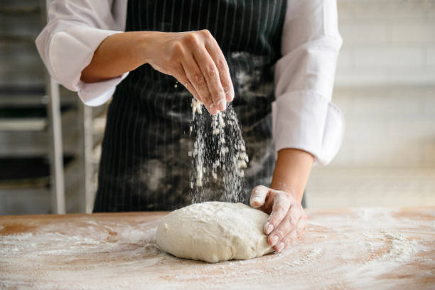 un boulanger saupoudrant la farine sur une pâte pour faire le pain - bread making photos et images de collection