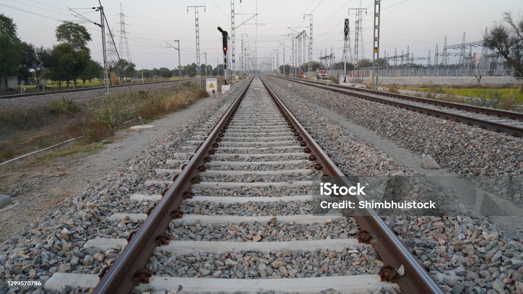 Long straight railroad from rusty rails on concrete sleepers in a rural area in the India. Cement sleeper or Block lay on the pebbles. The railway goes into the distance, beyond the horizon. The railway passes through wildlife. Railway, sleepers and rails in close examination. Sleepers and rails passing through wildlife. Architecture Stock Photo
