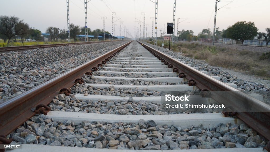 The railway goes into the distance, beyond the horizon. The railway passes through wildlife. Railway, sleepers and rails in close examination. Sleepers and rails passing through wildlife. Long straight railroad from rusty rails on concrete sleepers in a rural area in the India. Cement sleeper or Block lay on the pebbles. Architecture Stock Photo