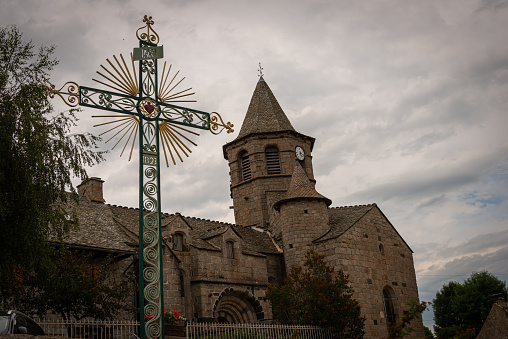 Nasbinals church with ornamental  cross in forground , cloudy skys , Lozere ,France .