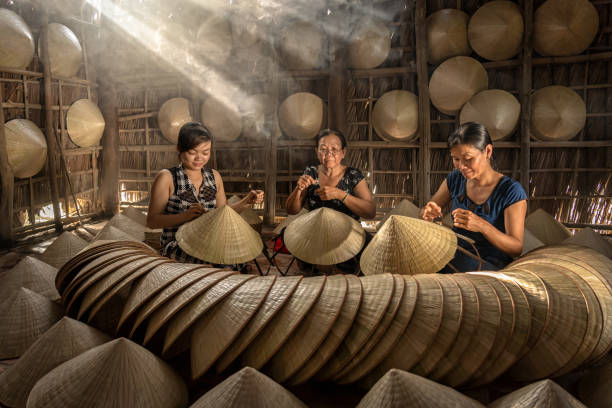 Group of Vietnamese female craftsman making the traditional vietnam hat in the old traditional house in Ap Thoi Phuoc village, Hochiminh city, Vietnam, traditional artist concept stock photo