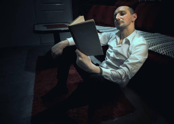 istock Man sitting on the floor reading a book in a cozy apartment 1299573182