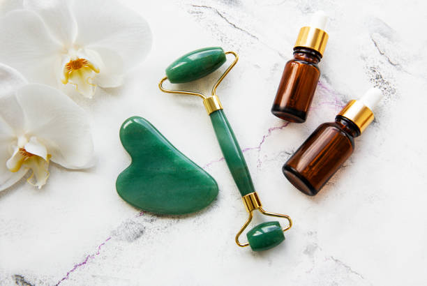 istock Face massage jade roller with cosmetic product on white marble background 1299573921