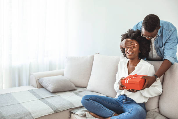 young couple with gift box hugging at home. - men african descent giving flower imagens e fotografias de stock