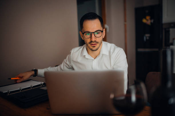 Work from home young businessman works from home in the evening and uses his laptop vollbart stock pictures, royalty-free photos & images