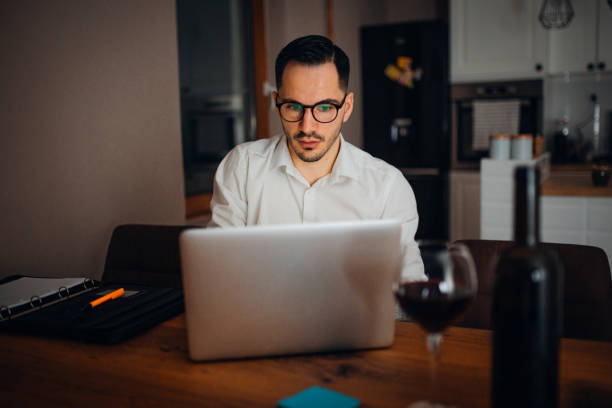 Work from home young businessman works from home in the evening and uses his laptop vollbart stock pictures, royalty-free photos & images