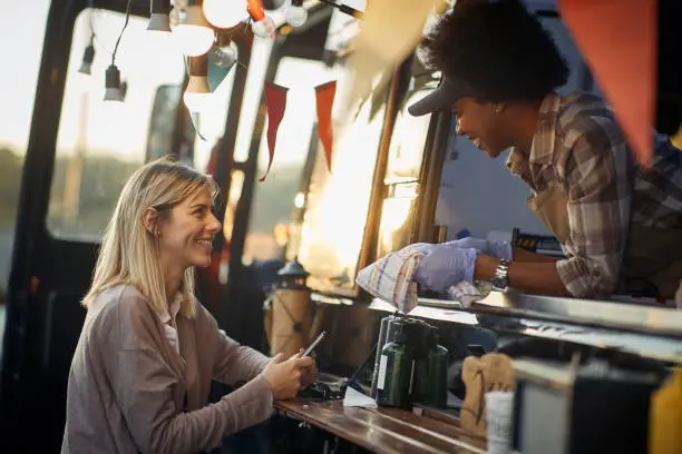 satisfied caucasian female customer talking with cheerful african employee on window of a modified truck for fast food