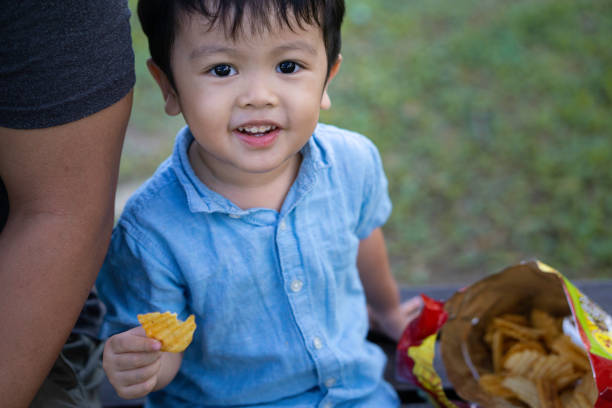 Adorable malay boy enjoying his snacks with his father at a public park stock photo