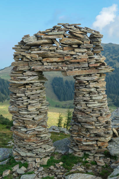 A stone made window, with the view on Packalpen, Austrian Alps. The stones are placed by humans, creating towers. The mountains around are lush green. Clear and bright day. Outdoor activity