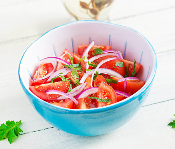 istock Fresh tomatoes with red onion and spices in a blue bowl.  Concept healthy appetizer. White wooden background. 1299598867