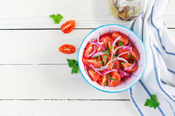 istock Fresh tomatoes with red onion and spices in a blue bowl.  Concept healthy appetizer. White wooden background. Top view, copy space 1299598868