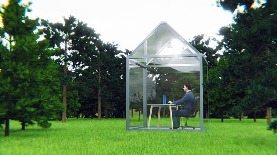 Concept of working secure from anywhere if you just have your laptop with you. Table and chair stands in the middle of a green house made of glass.