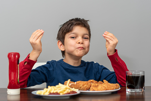 little boy is eating fried chicken with cola and french fries