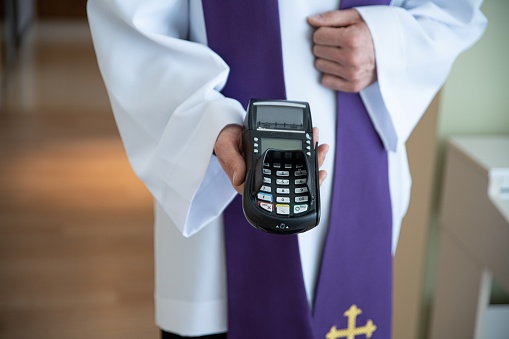 Card reader in the hand of a priest during a pastoral visit. Greed in the Polish church.