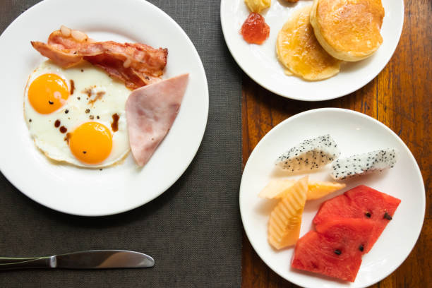istock Delicious breakfast; sunny-side-up fried egg, ham, bacon, pancakes with fruits; on wooden table. Top view. 1299602921