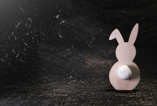 silhouette of a wooden rabbit with a white tail on a black background, dust, Easter background
