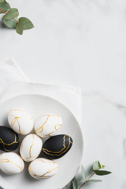 istock Luxury Easter eggs decorated with gold in plate and eucalyptus leaves on marble table. Flat lay, top view. Minimal style. 1299603349