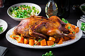 Homemade baked duck. Crispy whole roast duck. Thanksgiving or Christmas dinner. Roast duck with thyme and pumpkin on rustic wooden table.