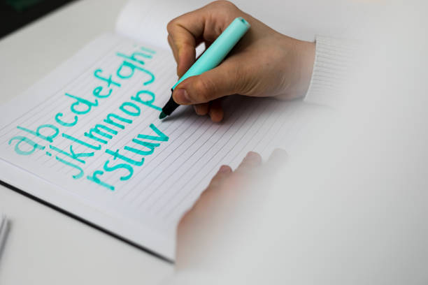 Girl sitting down and drawing the alphabet with a blue marker.