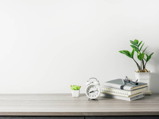 istock Workspace with book, clock and tree pot on wood table with living room white wall 1299605637
