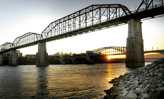 The sun sets behind Walnut Street Bridge and Market Street Bridge in Chattanooga, Tennessee over the Tennessee River.