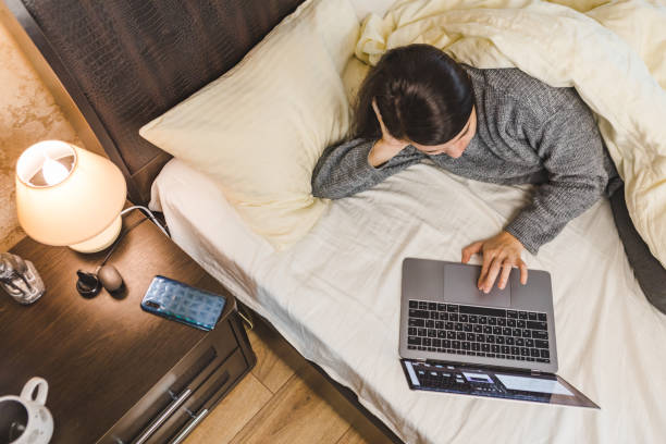 istock woman laying down in bed working on laptop 1299608287