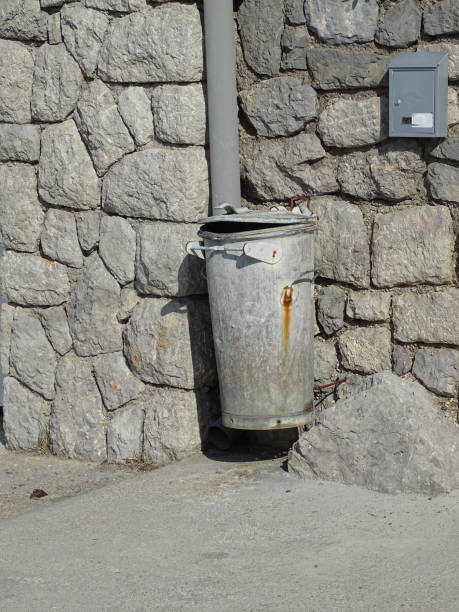 istock Garbage can old metal on a natural stone wall 1299609338