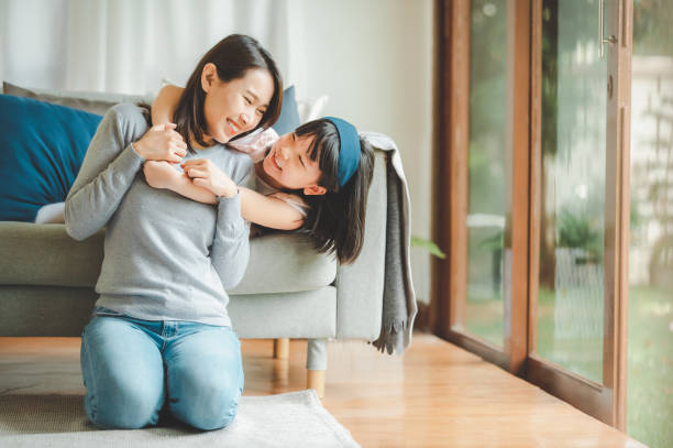 Happy Asian mother and cute little daughter having fun Happy Asian mother and cute little daughter having fun while playing and hugging at home in living room asian daughter stock pictures, royalty-free photos & images