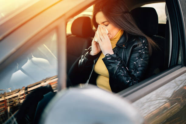 istock Young woman driving car with protective mask on her face 1299612098