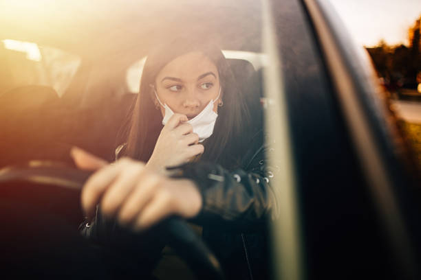 istock Young woman driving car with protective mask on her face 1299612226