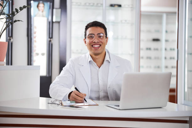 istock Smiling bespectacled optometrist seated at the table in his office 1299614834