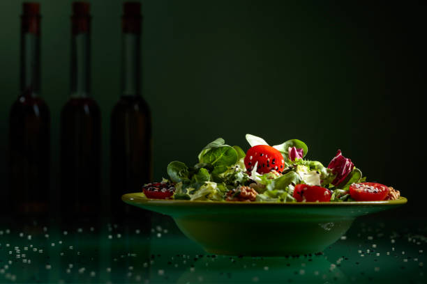 Green salad with cherry tomatoes, walnuts and vegetable oil sprinkled with sesame. In the background, silhouettes of olive oil bottles.