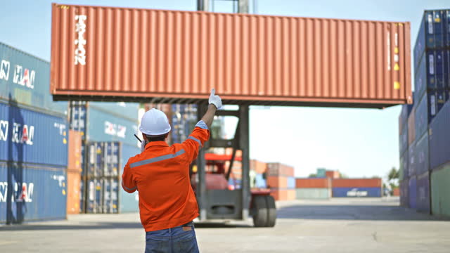 4K Male Dock Worker Using A Radio Telling Top Handler Moving Containers In Shipping Dock